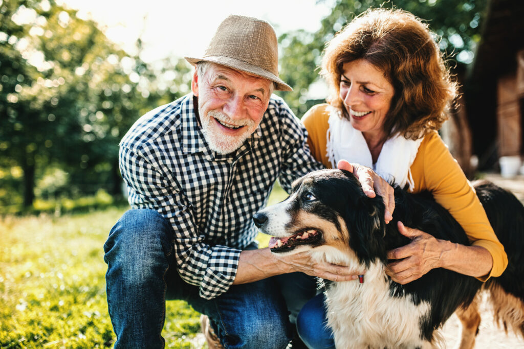An older couple smiling and playing with their dog outside.